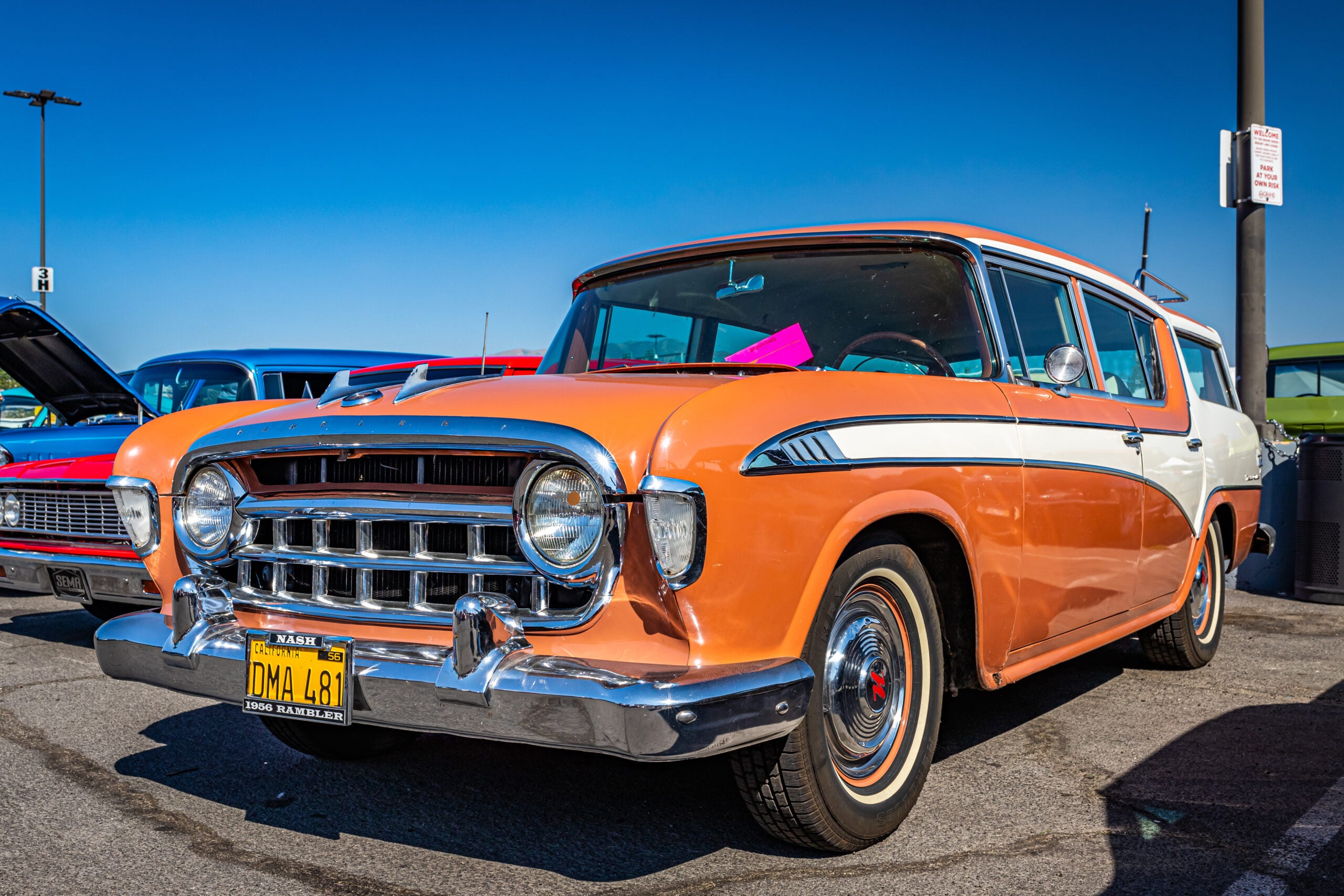 A orange and white Nash Rambler is parked in a lot.