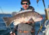 Fisherman holds a tautog fish on a boat in winter.