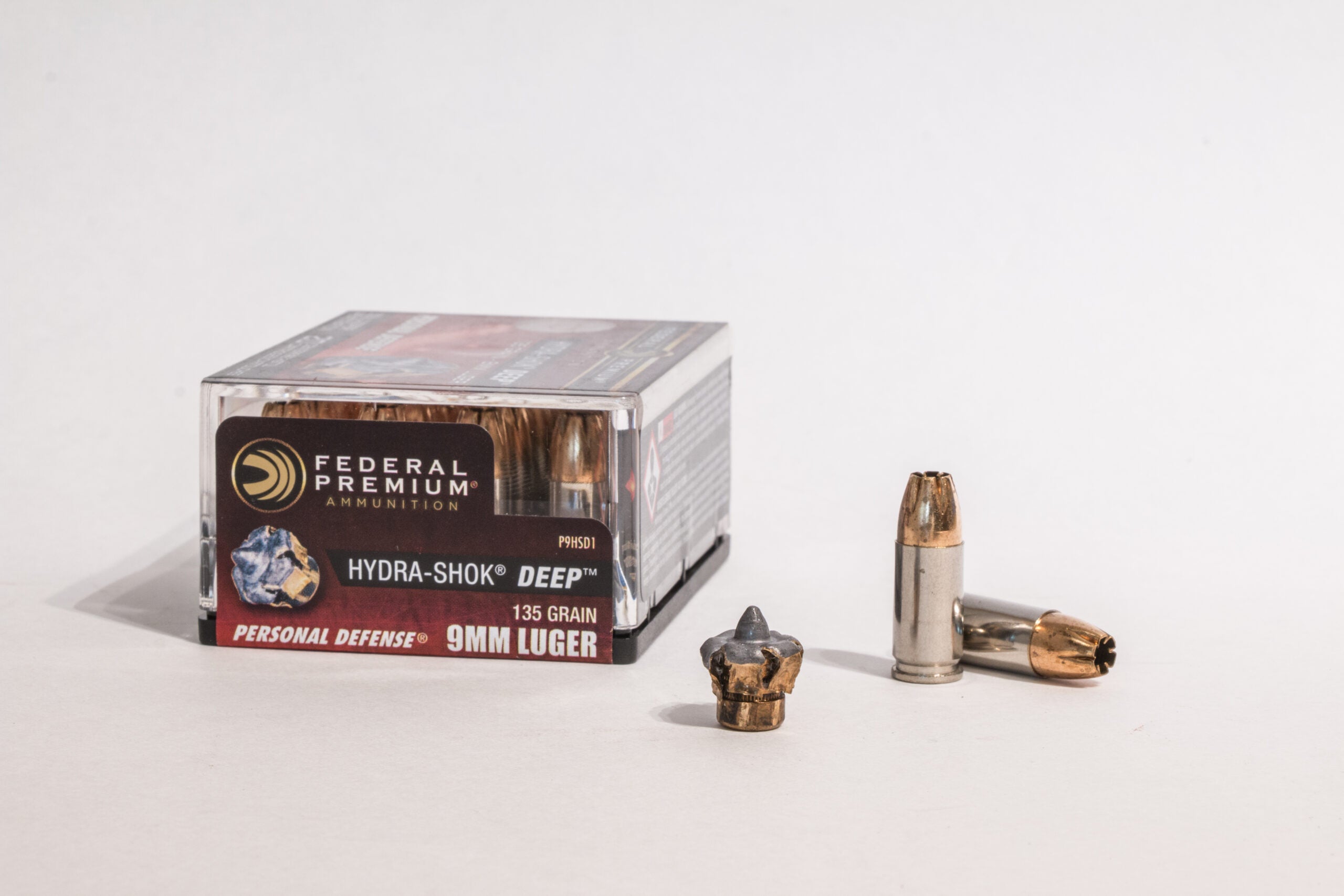 Box of 9mm Luger ammo with one fired bullet and two loose cartridges on white background