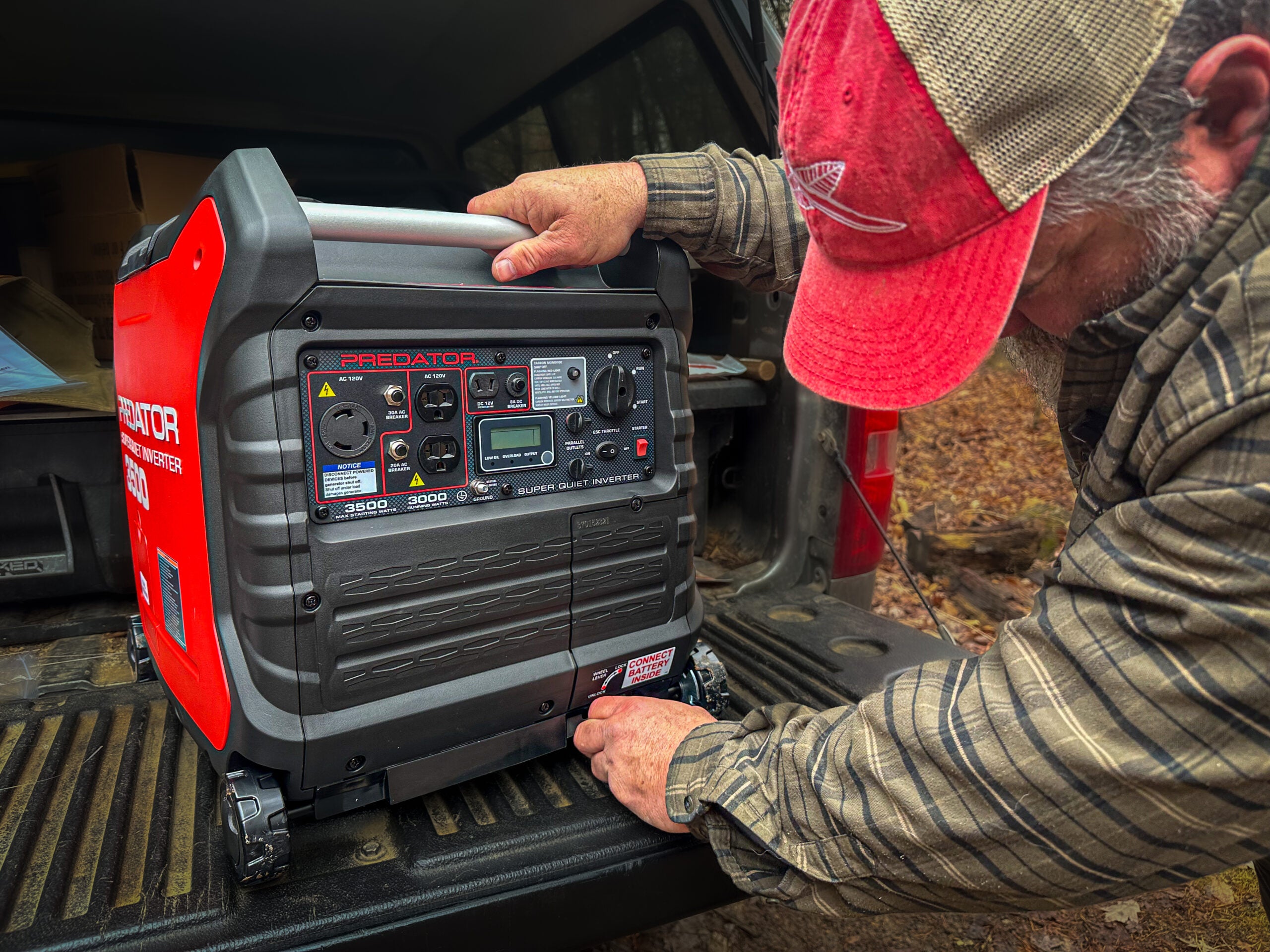 A person in a red and white hat checks an inverter generator on his tailgate.