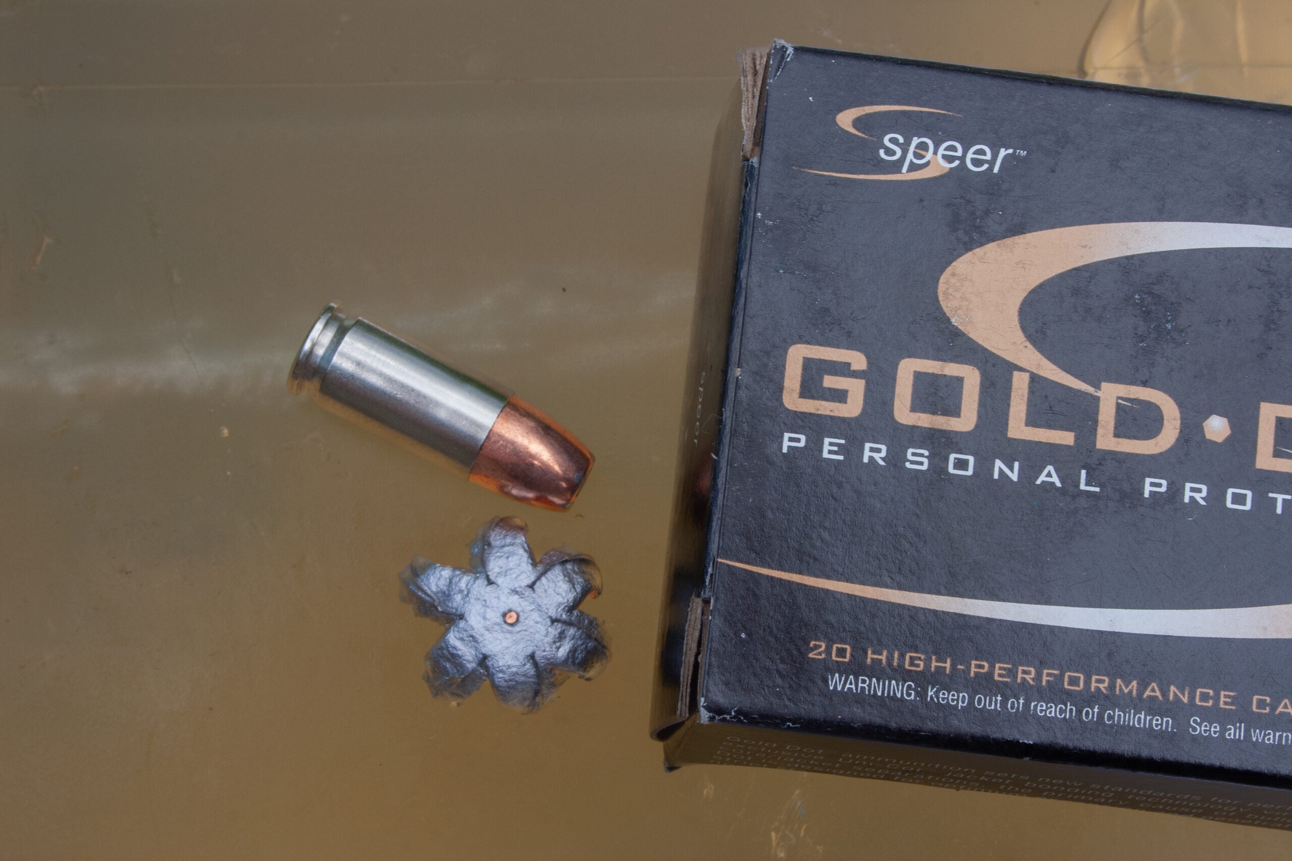 Box of 9mm ammo, fired bullet, and unfired cartridge sit atop a block of ballistics gel