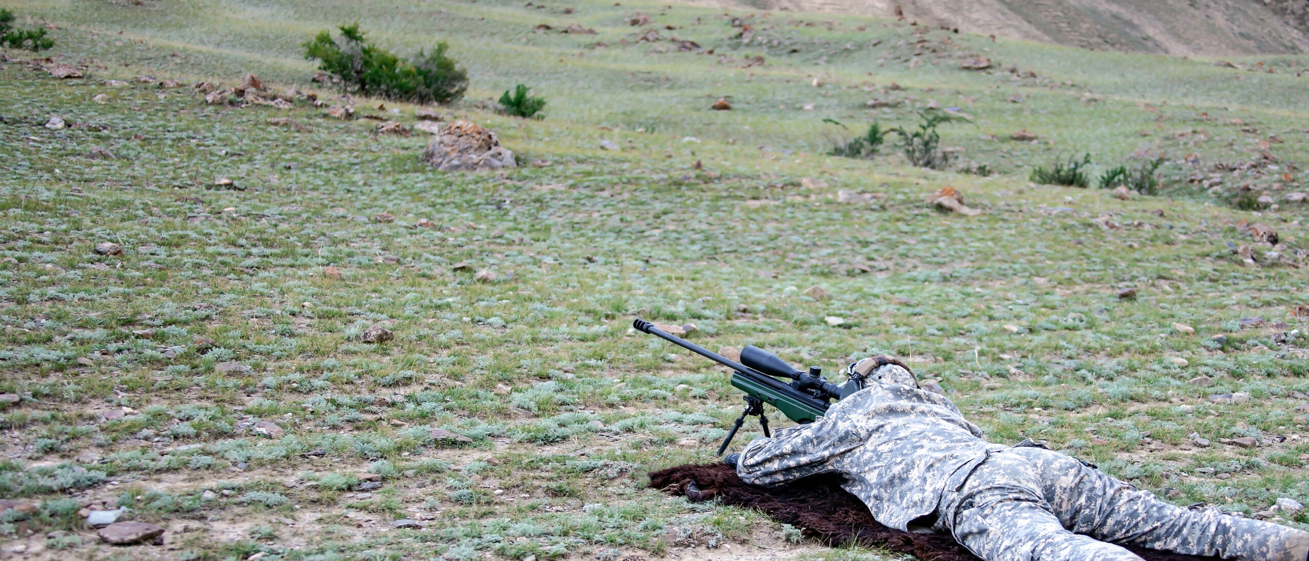 A shooter fires a long range rifle from the prone position in a field