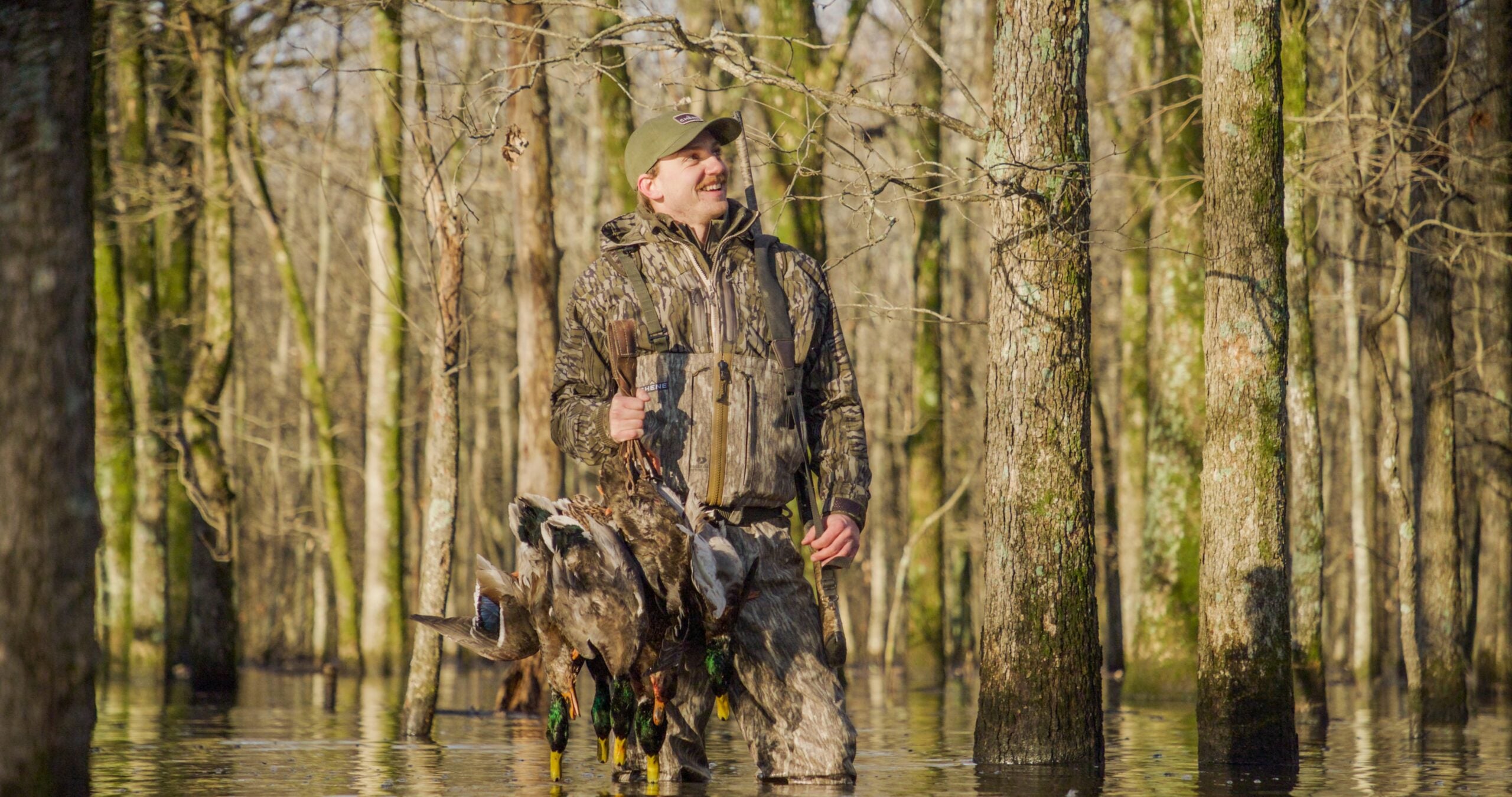 hunter holding strap of mallard ducks in flooded timber