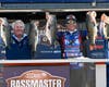 Pro bass fishermen hold of fish at the podium of a recent Bassmasters event