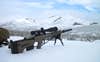 A heavy long-range rifle propped on a bipod in the snow with mountain vista in background