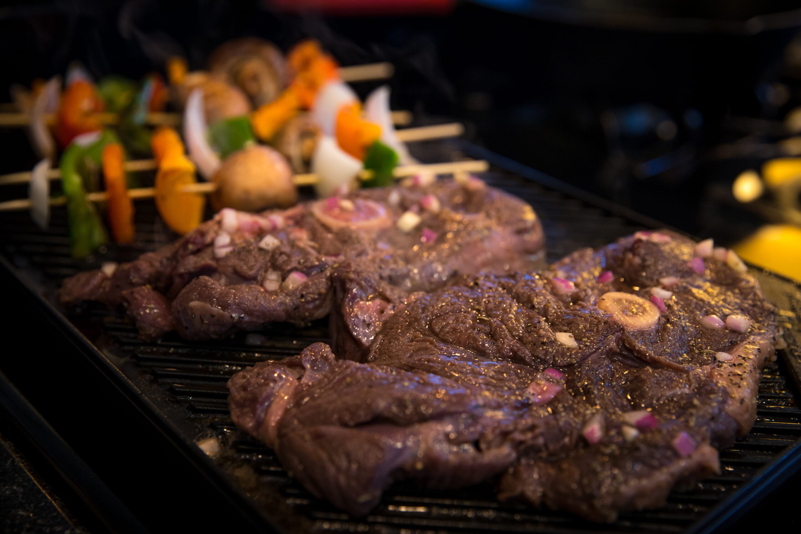 Bear steaks cooking on a grill with vegetable skewers in background