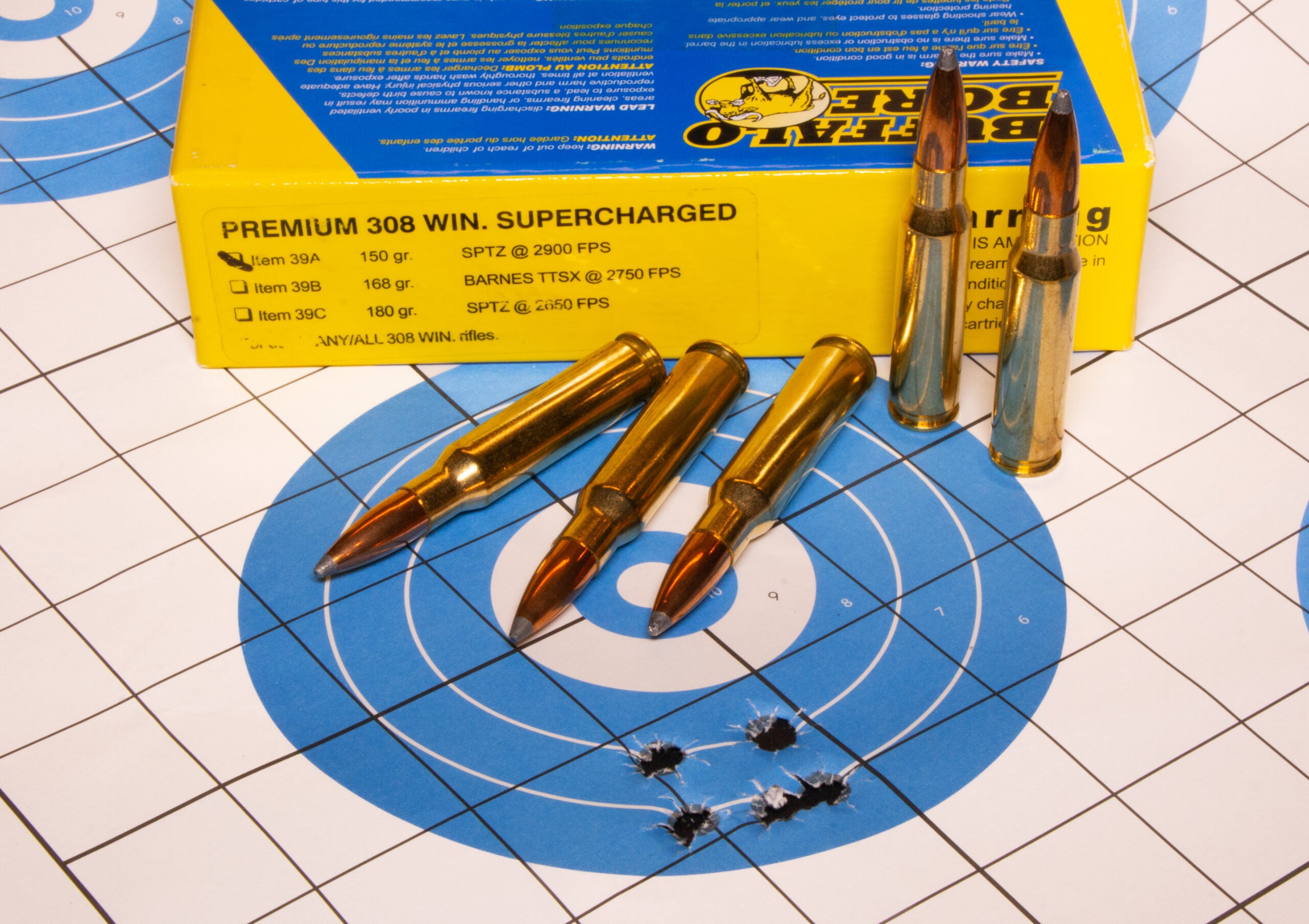 A target with five bullet holes, a box of ammo, and five loose cartridges