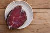 A slice of raw venison sits on a white plate resting on a wooden table.