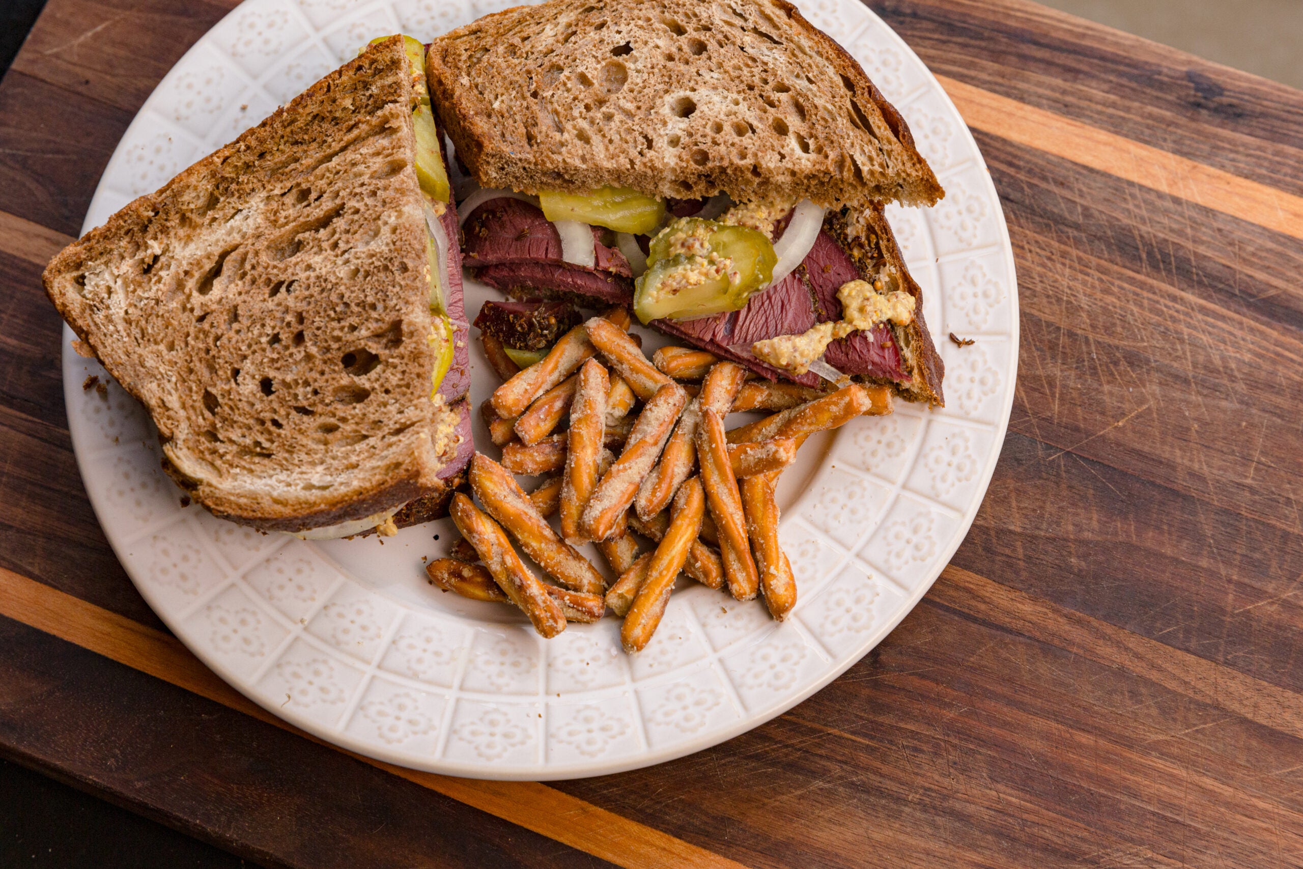 A venison pastrami sandwich on a white plate with a side of pretzels.