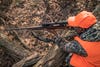 A man wearing orange shoots a rifle while leaning against a fallen log