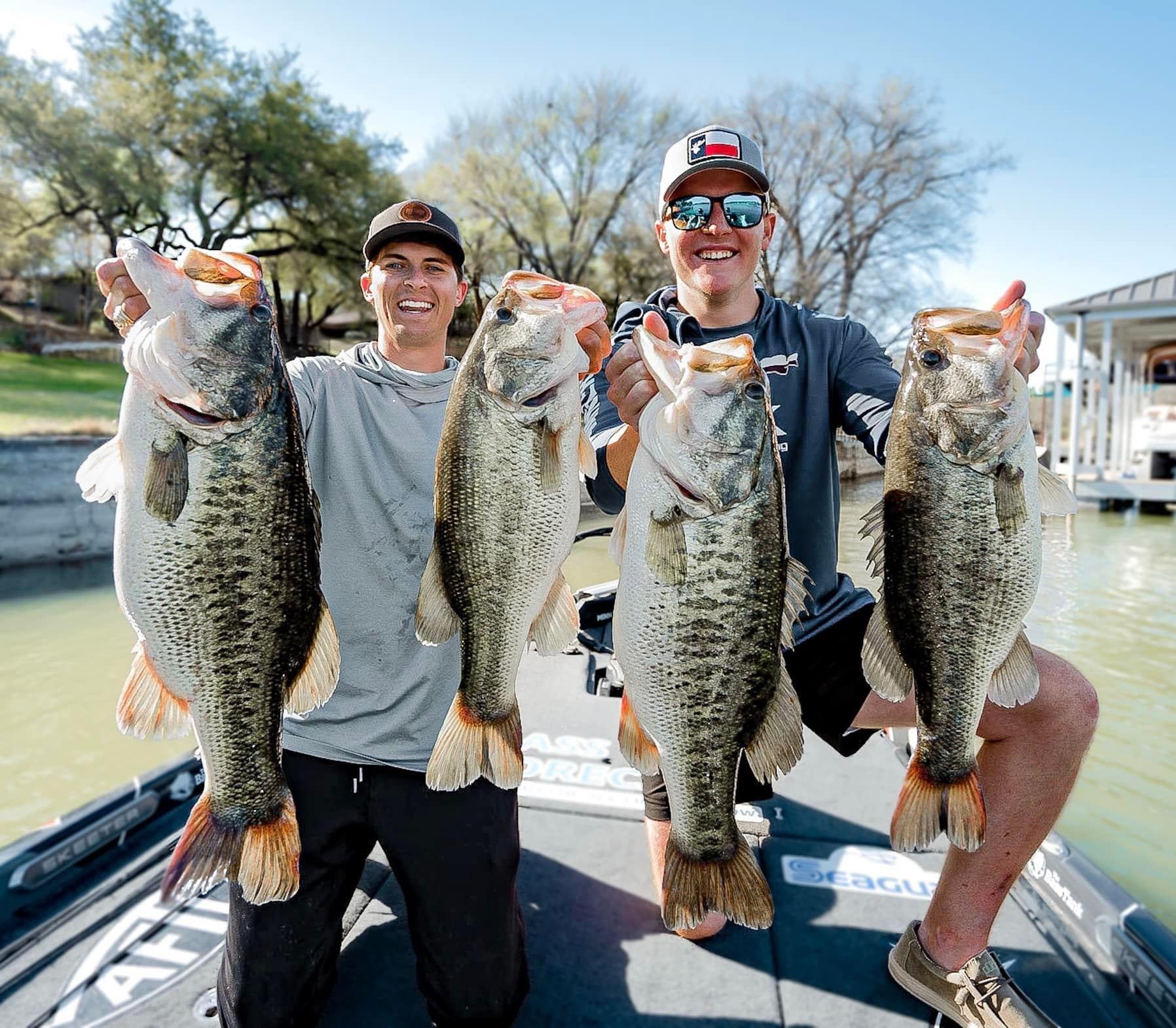 Two anglers in a boat each hold up two big largemouth bass they've caught