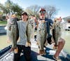 Two anglers in a boat each hold up two big largemouth bass they've caught