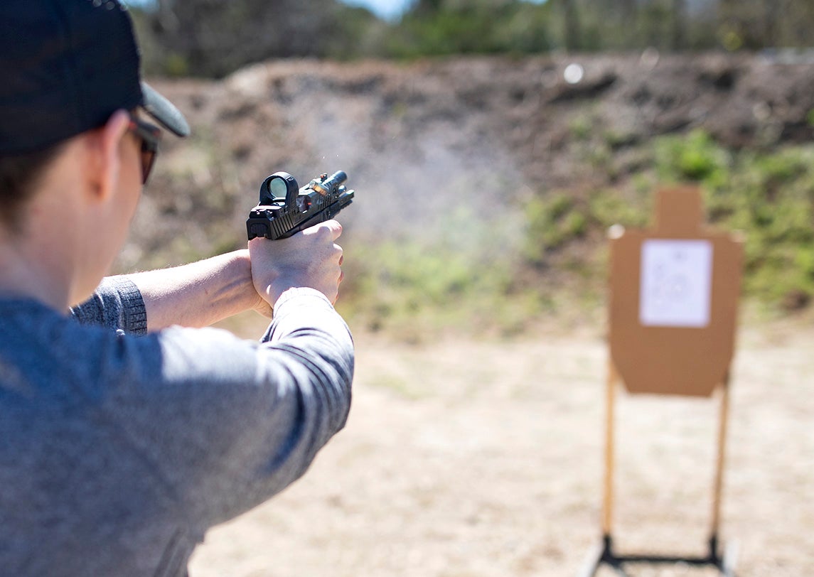 A person on a shooting range firing a pistol with an SRO red-dot sight.