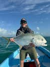 a fly fisherman in a black hat and hoodie holds a jack crevalle
