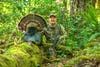 Oregon turkey hunting expert Scott Haugen poses with a tom turkey in deep spring woods.