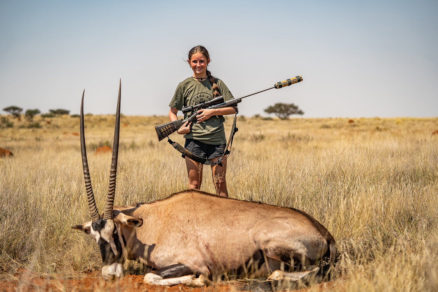 Young woman hunting with a suppressor standing over an African gemsbok.