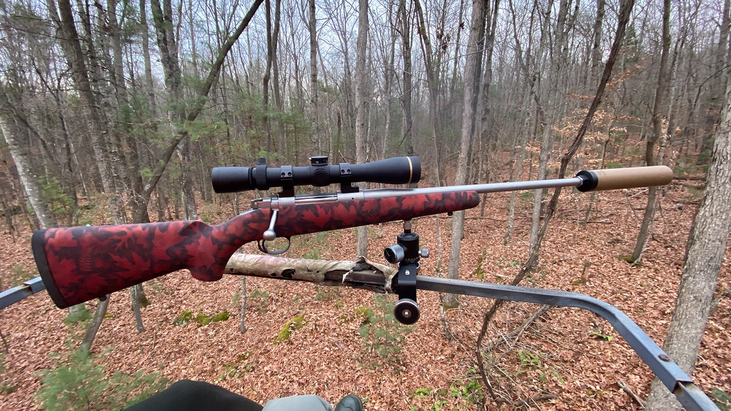 A Kimber rifle with suppressor attached to a tree stand rail.