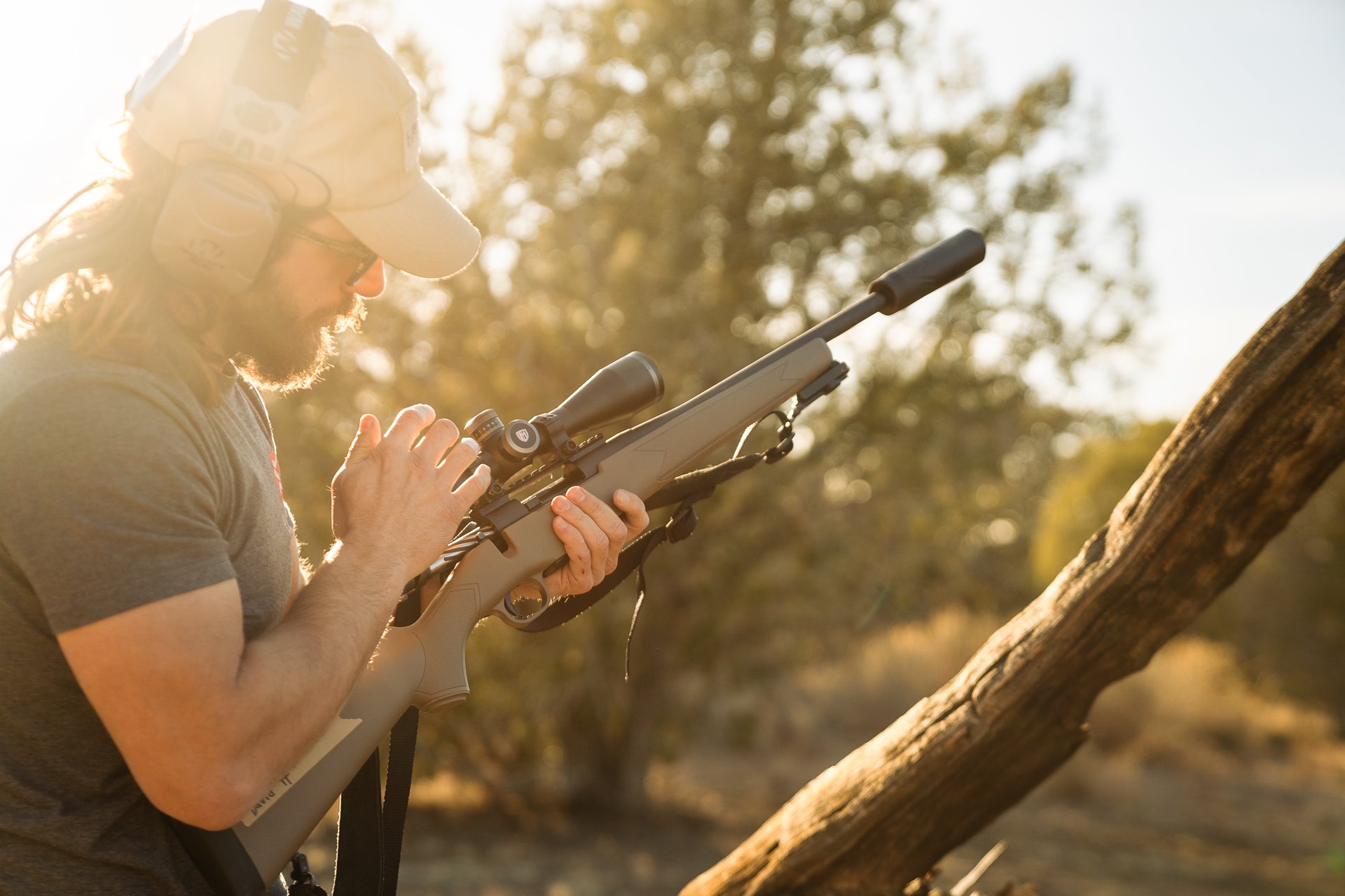 A shooter works the bolt of a suppressed Mossberg rifle.
