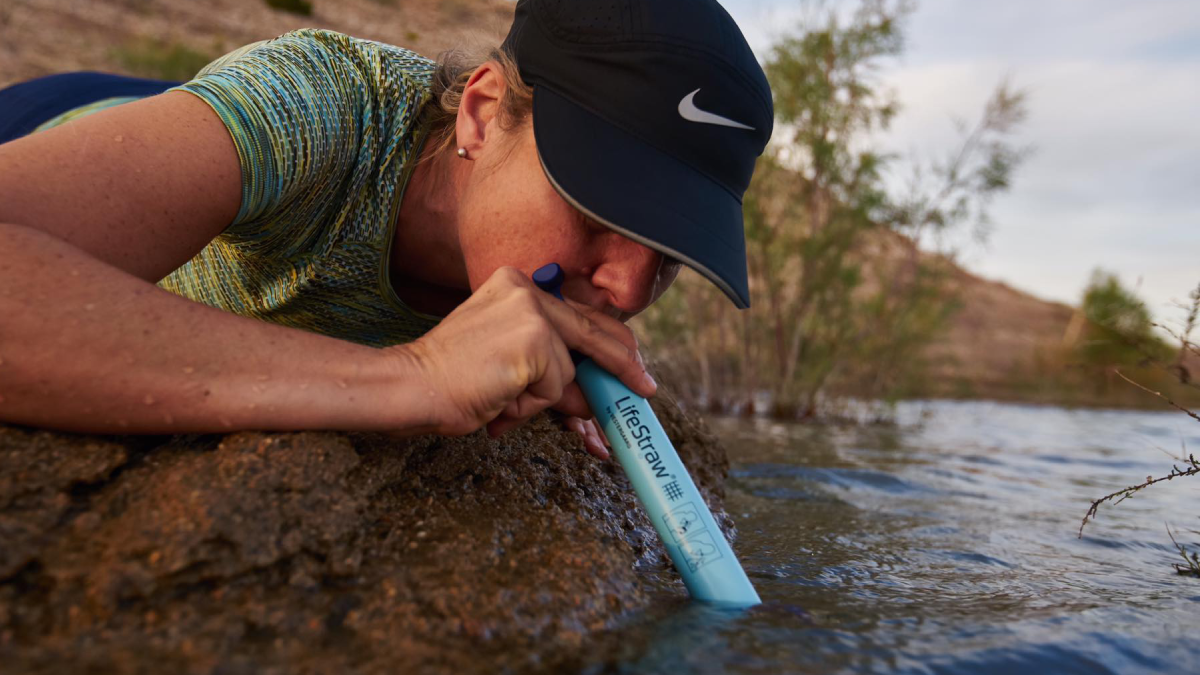 Woman using Lifestraw Personal Water Filter to drink from stream