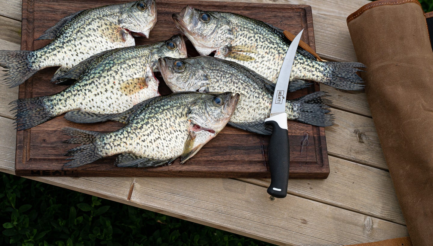 Six crappie on a wooden cutting board with a fillet knife next to them