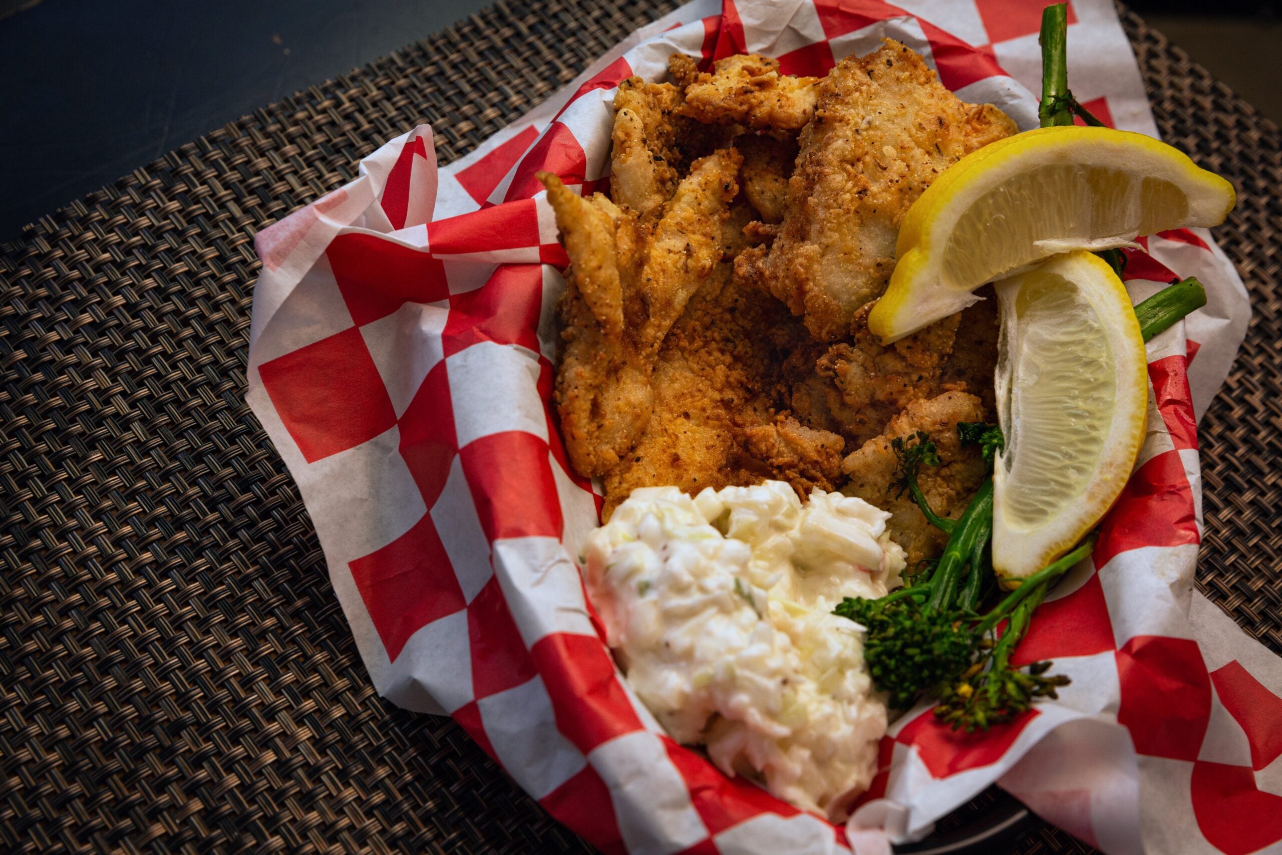 A basket of fried catfish with slaw and lemon wedges