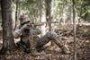 A turkey hunter sitting again a tree trunk in the woods aim his shotgun.