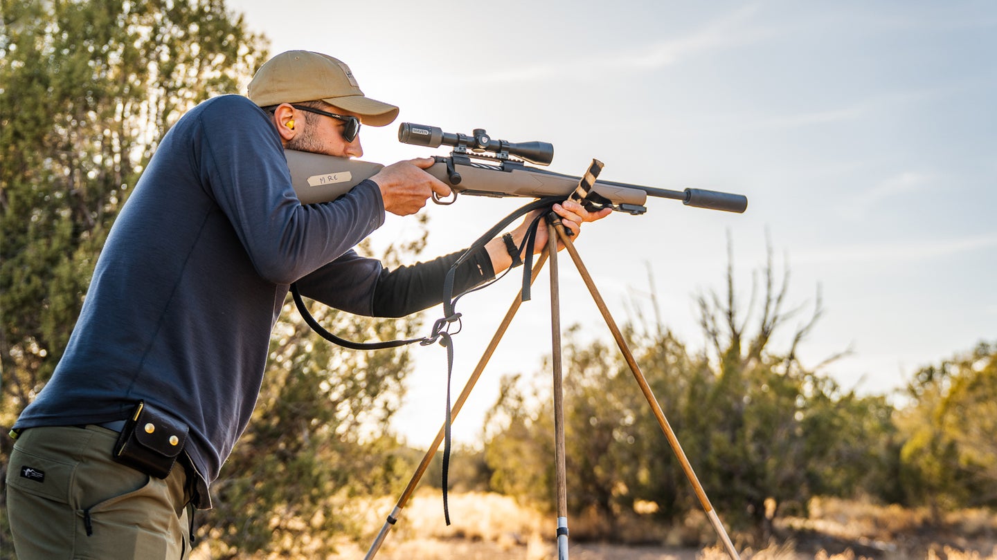 A shooter takes aim with a rifle resting on shooting sticks.