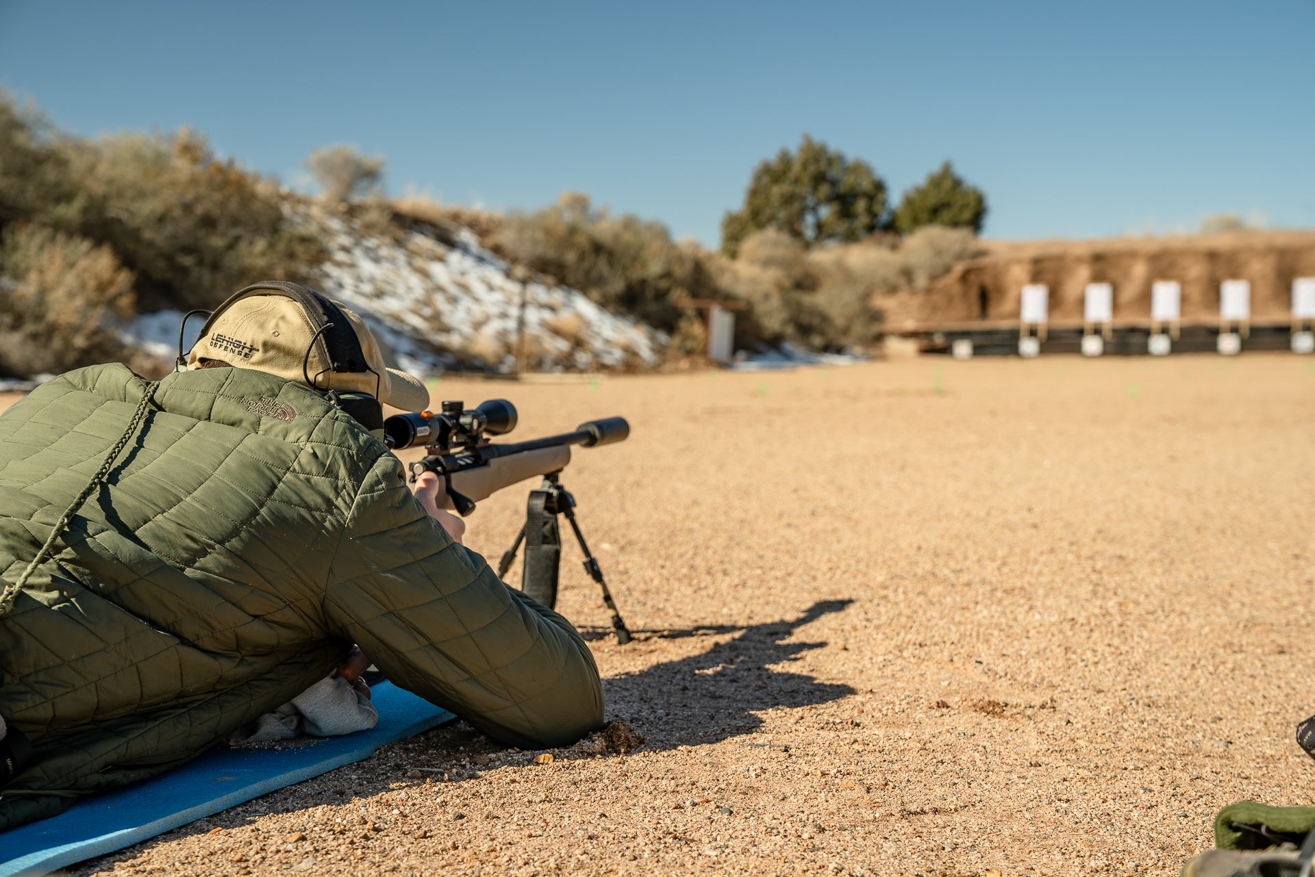 A rifle shooter lying prone and aiming a row of targets at a shooting range.