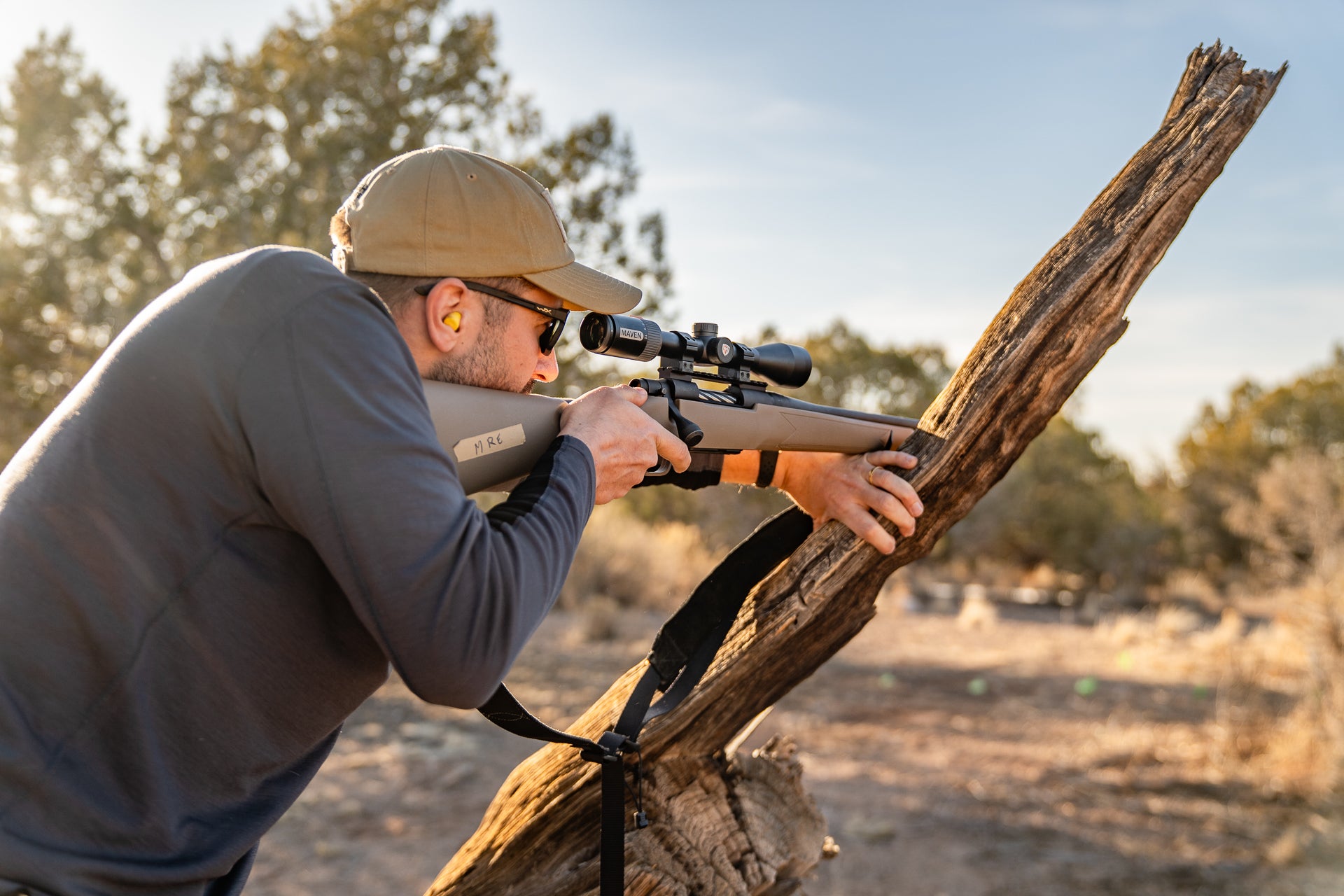A shooter takes aim with his rifle resting on a tree limb.