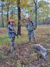 Two female hunters look at a dead deer on the ground