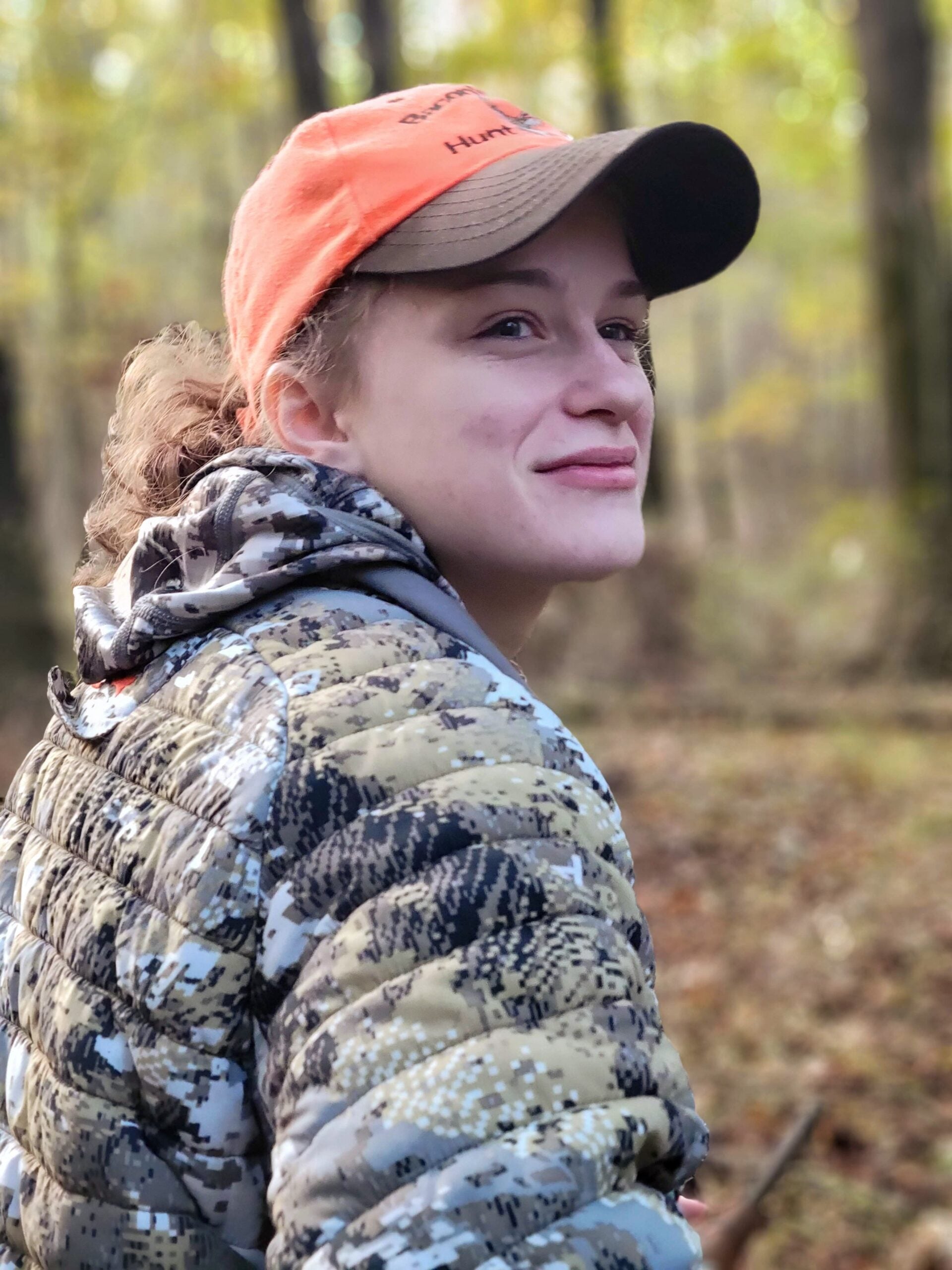 A young female hunter dressed in a camouflage coat and an orange hat