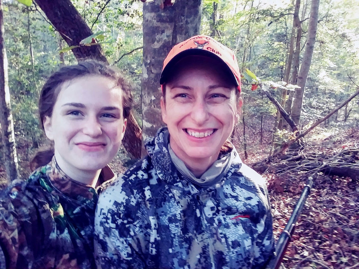 A mother and her daughter dressed in camouflage in the woods.