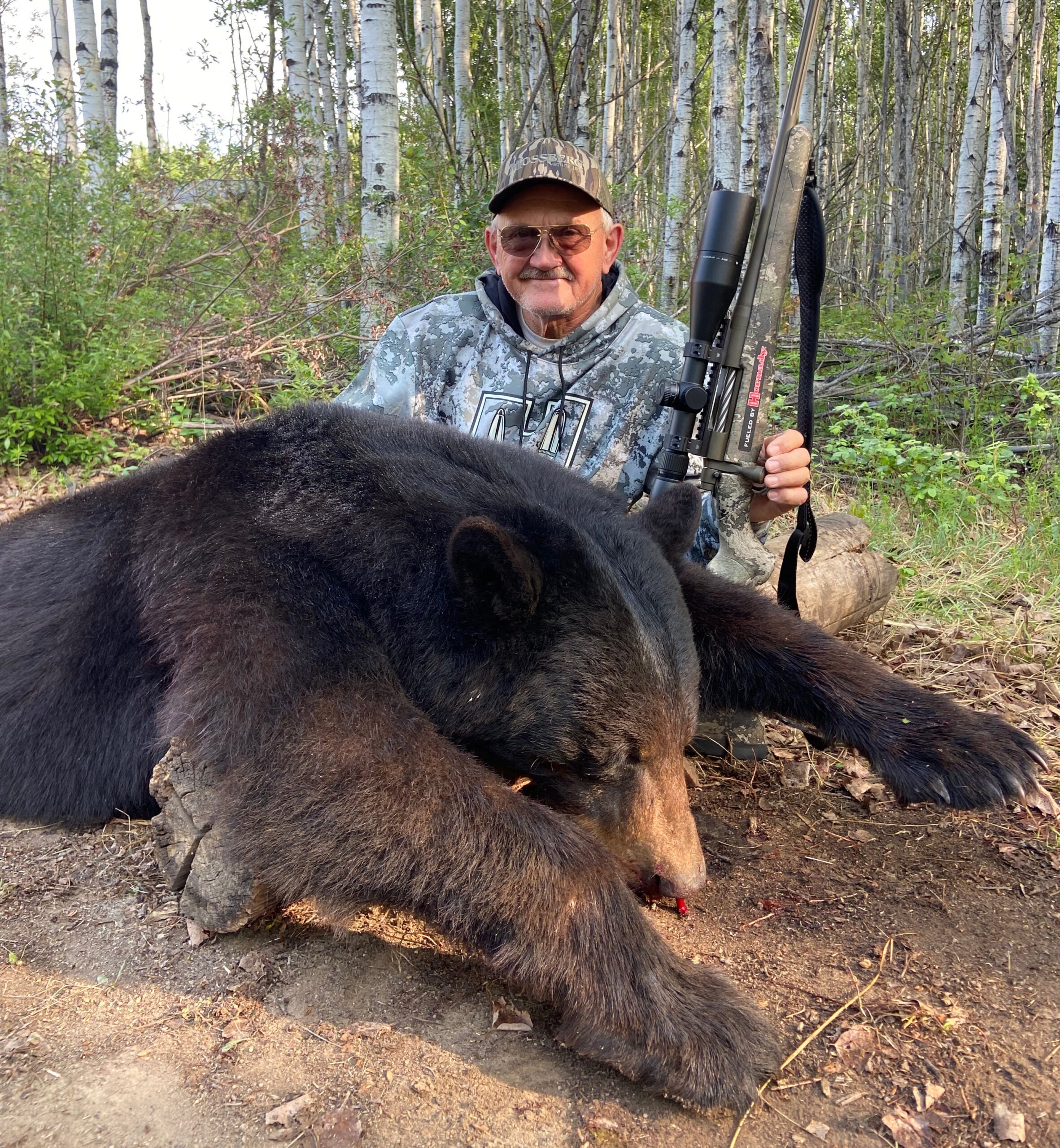 Pro shooter Jerry Miculek, holding a rifle, poses with a black bear he took in Canada.