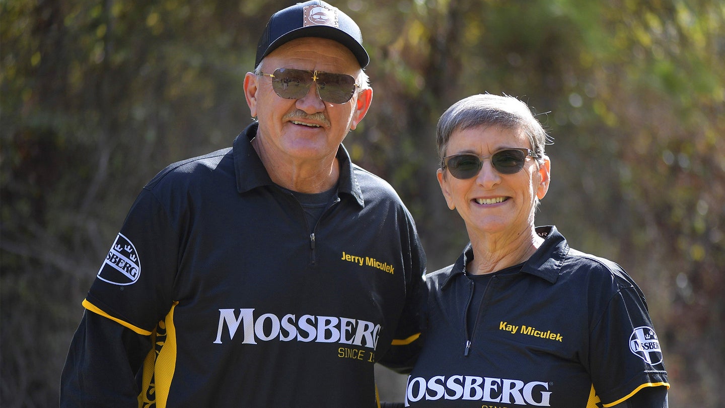 Pro shooters Jerry and Kay Miculek, wearing Mossberg tee shirts, pose in an outdoor setting.