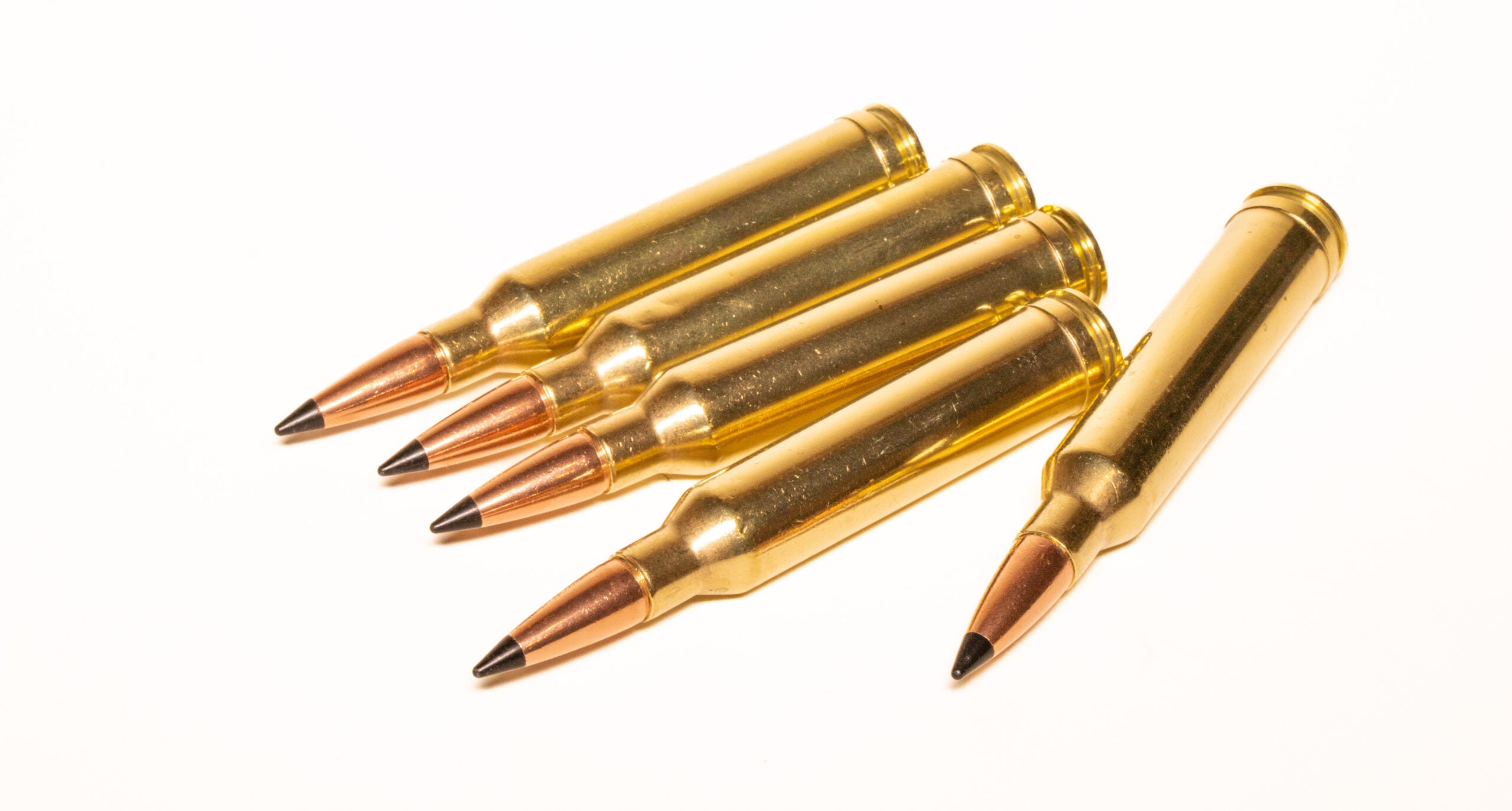 Five 7mm Rem Mag cartridges on a white background.