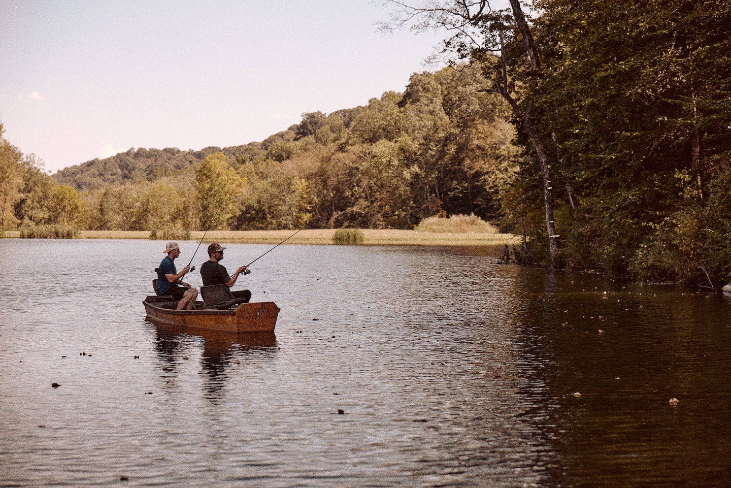 Two fishermen bass fish from a canoe on a pond